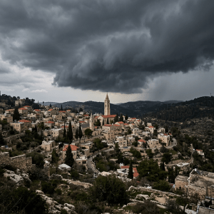 Hillside village with stone buildings and church tower under dark storm clouds